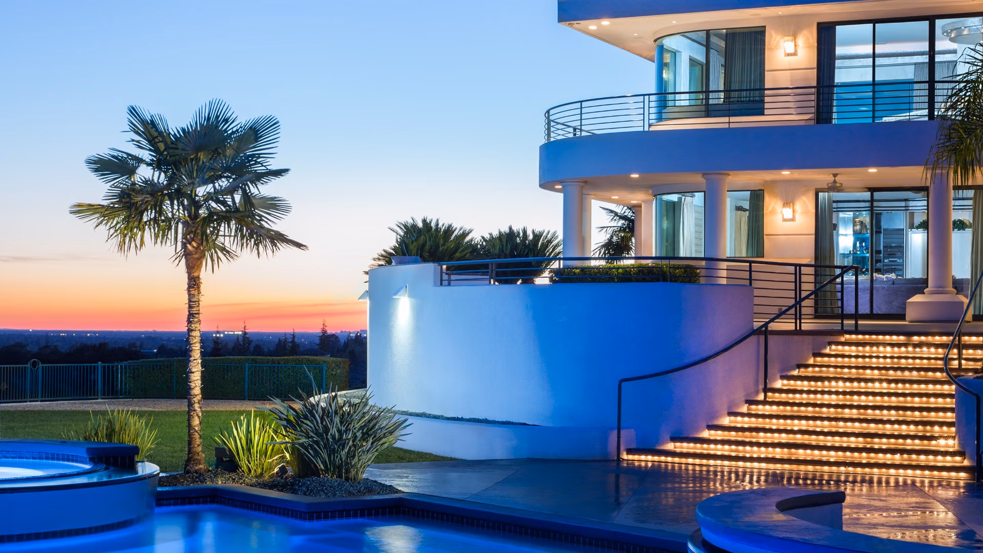 A contemporary estate in Granite Bay at dusk, with a lit terrace and pool overlooking the valley