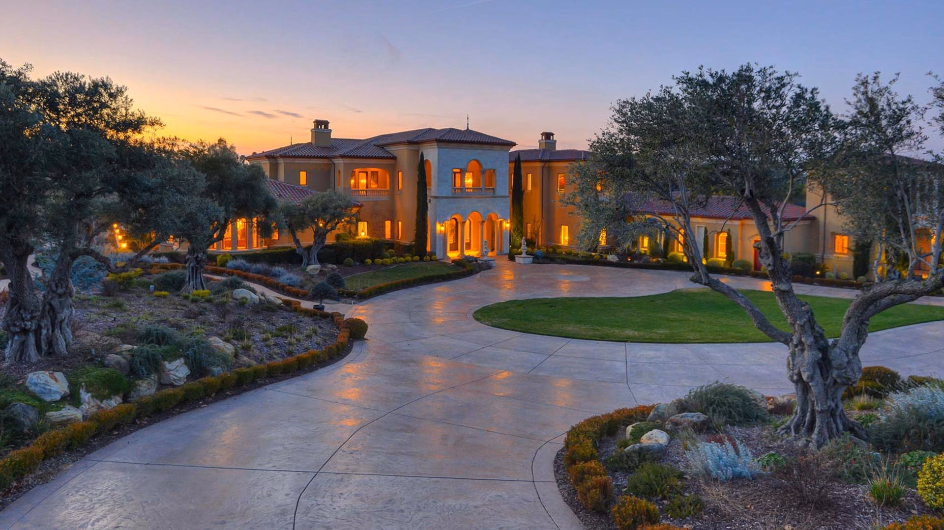 A Mediterranean-style estate at twilight with olive trees and a circular drive